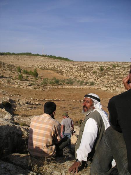 Za palestinskými farmáři je vidět řada polí ve Vádí, které je předmětem sporu. Zelený vrcholek hory je hranicí židovské usedlosti Maon.